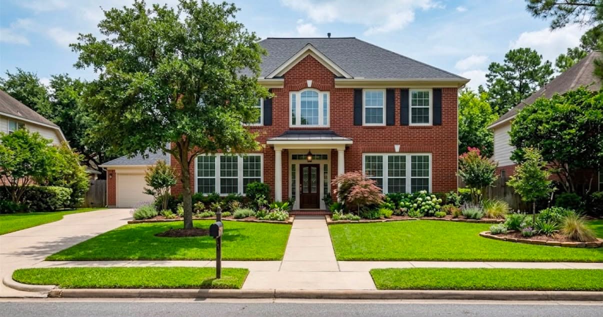 Foundation beds and lawn care: trimmed shrubs along the front of a red brick home, an edged lawn and a central walkway