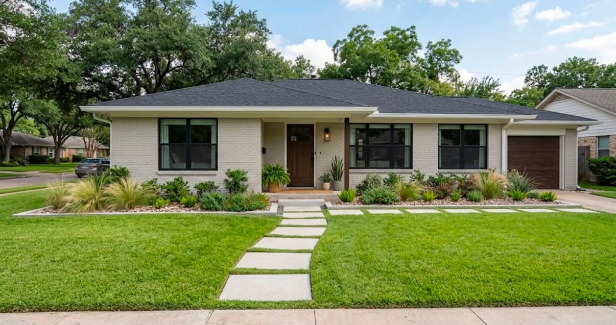 Modern front yard design: concrete stepping pads across the lawn, ornamental grasses and gravel beds at a white brick ranch home