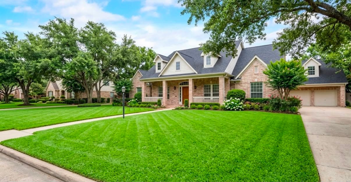 Wide front lawn with fresh mowing stripes and mature shade trees in front of a stone and brick home